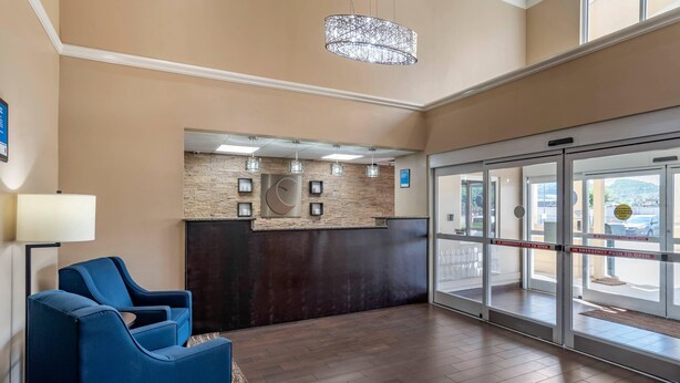 A reception area with a dark reception desk, a blue sofa, and a chandelier. - Comfort Inn Birmingham - Irondale (Birmingham)