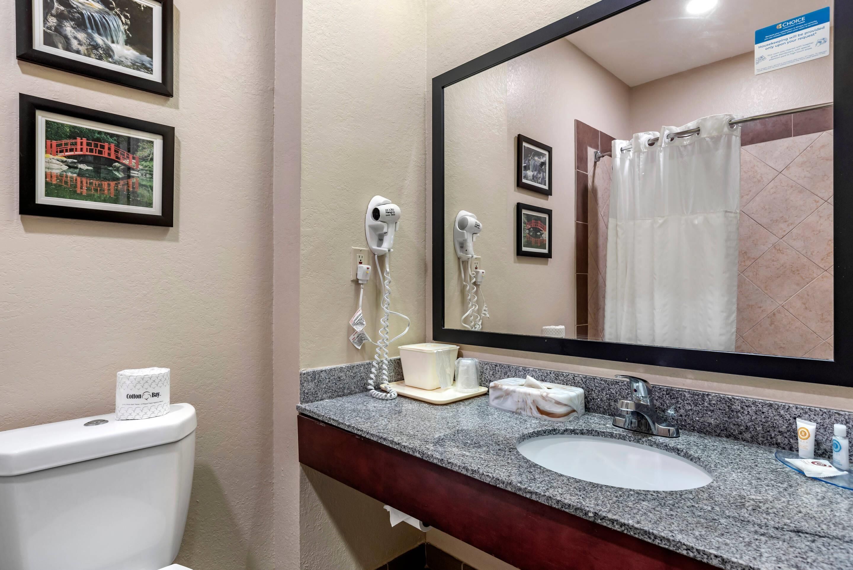 Un baño con lavabo, espejo y dos secadores de pelo fijados en la pared.