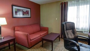 Une chambre d’hôtel avec un canapé rouge, un fauteuil de bureau noir, une petite table et une lampe.