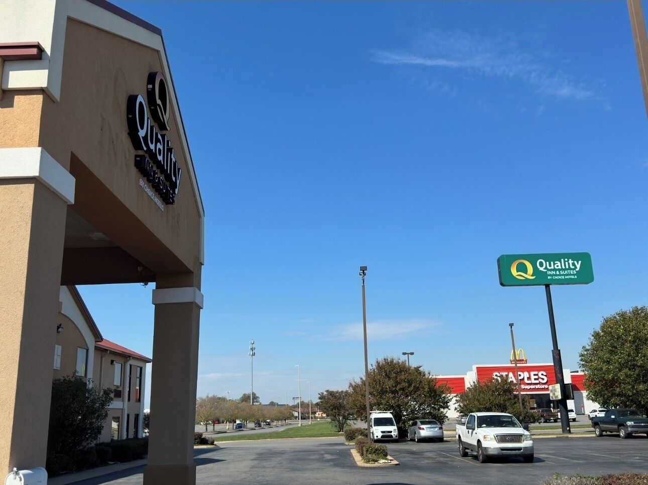 Skilt for Quality Inn & Suites, en McDonald's og en Staples butik i en parkeringsplads.