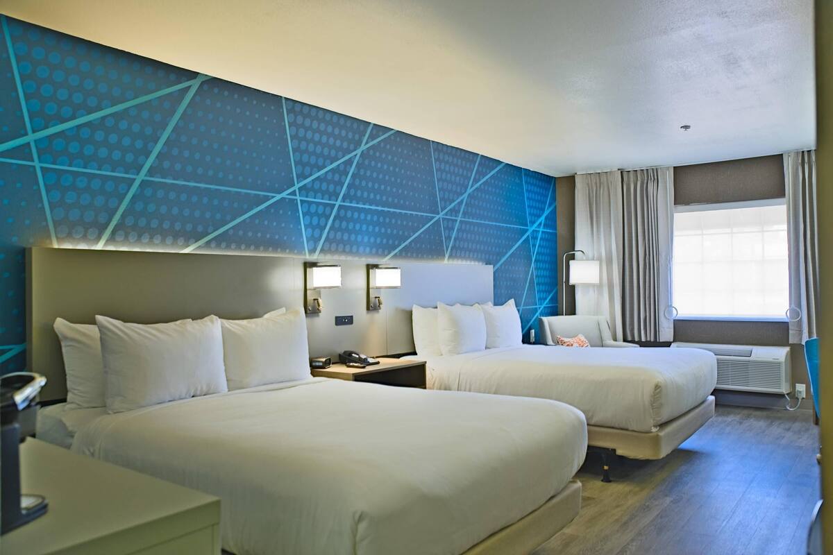 A hotel room with two beds, a desk, a phone, and a window with curtains.