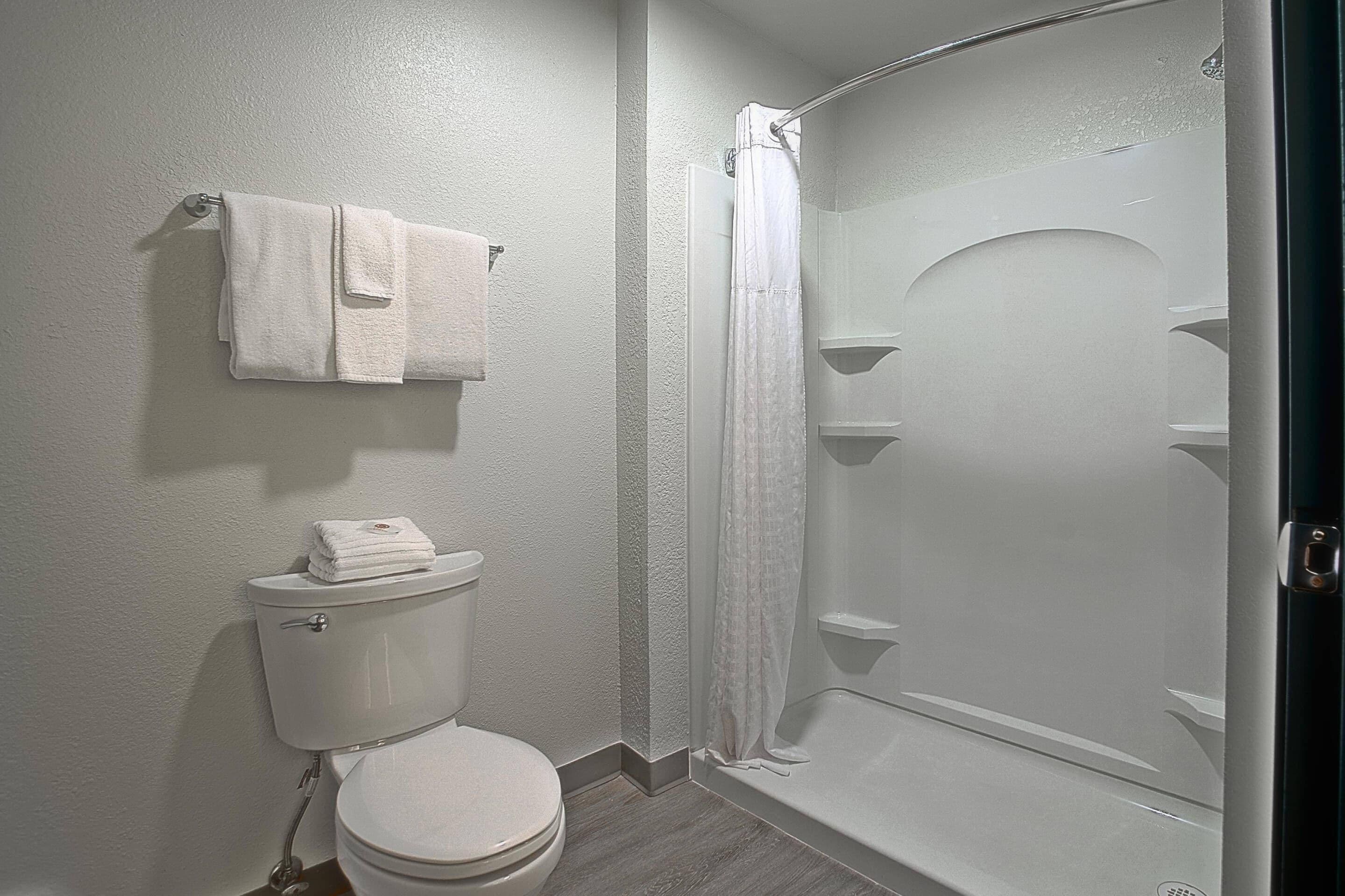 A bathroom with a toilet, a shower with a glass door, and a towel rack with towels.
