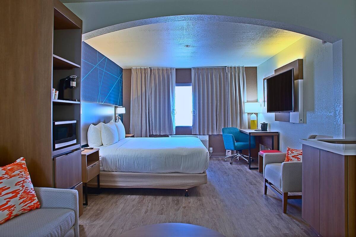 A hotel room with a bed, desk, chair, TV, and a minibar.