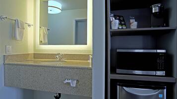 A bathroom with a sink, mirror, towel rack, and a microwave on a shelf.