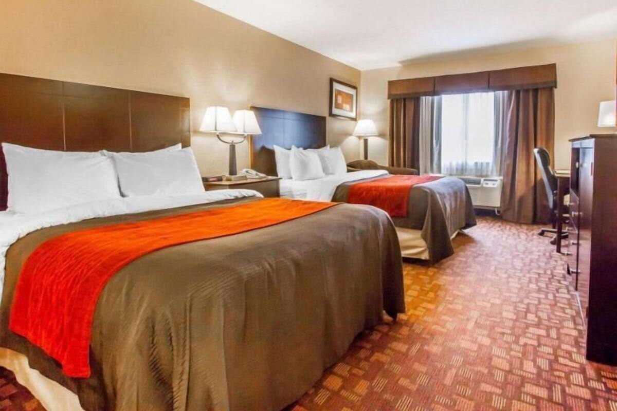 A hotel room with two beds, a desk, a chair, and a window with curtains.