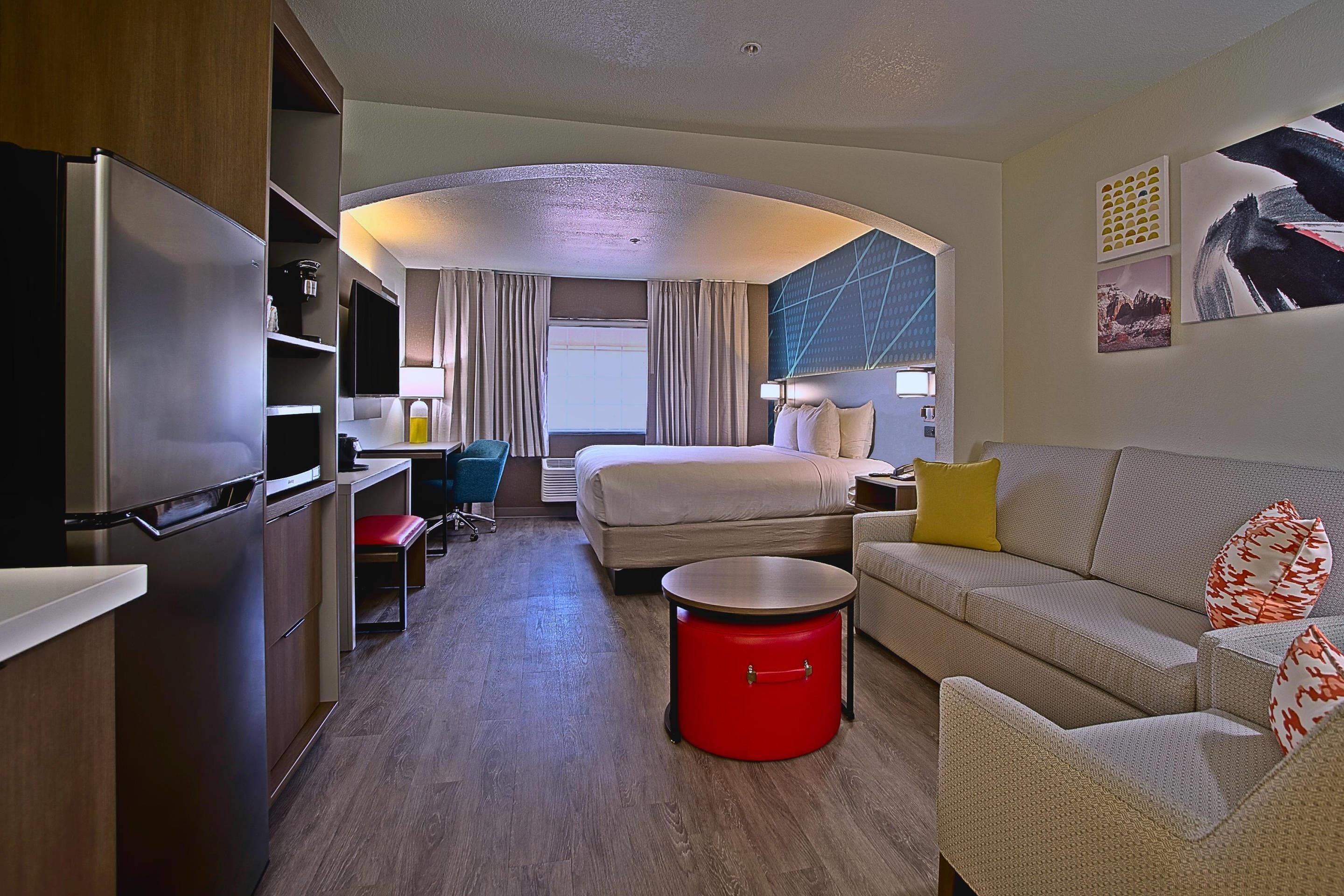 Ein Hotelzimmer mit einem Bett, einem Sofa, einer roten Mülltonne, einem Schreibtisch mit Stuhl und einem Fernseher.