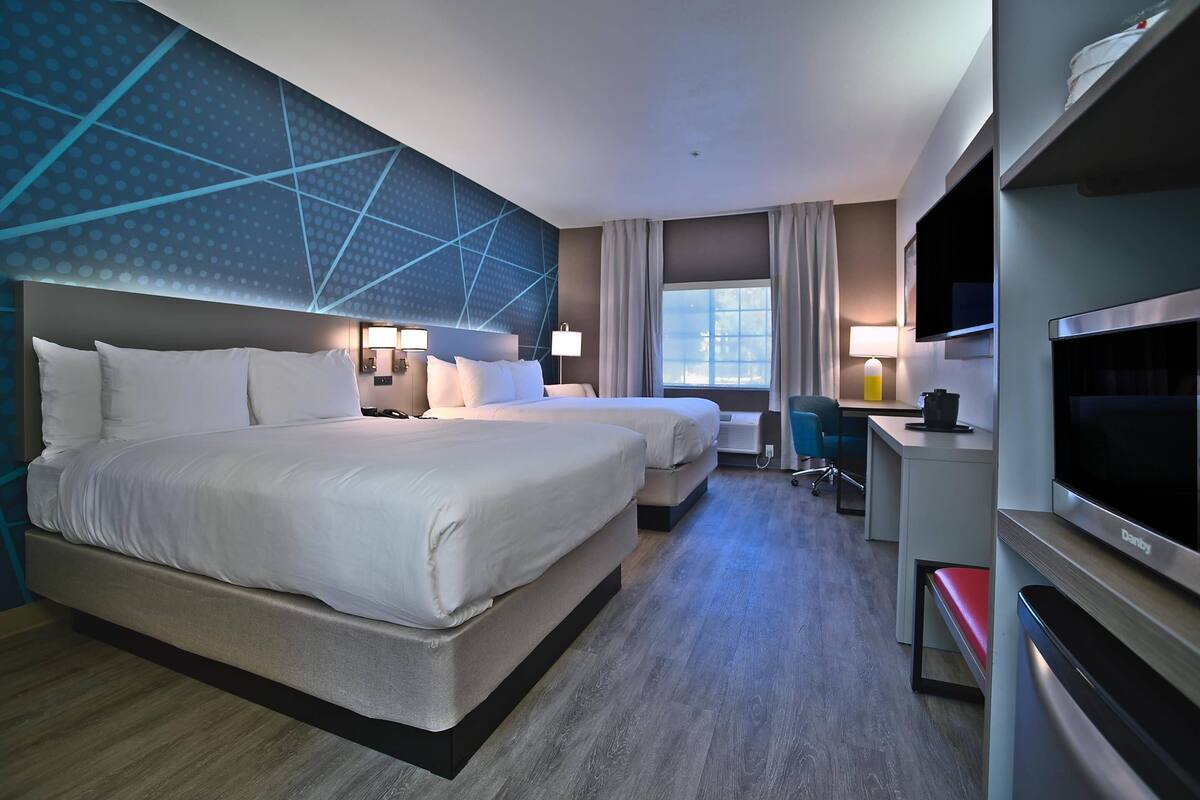 A hotel room with two beds, a desk, a TV, and a large window.