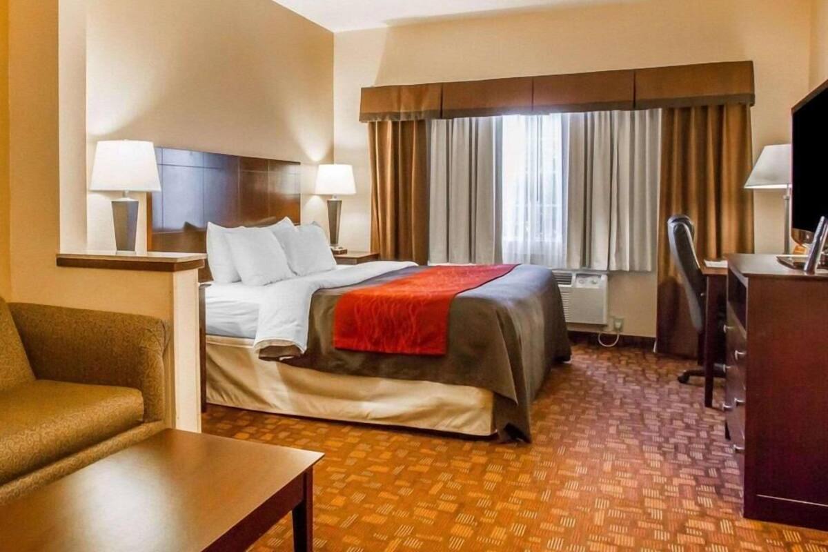 A hotel room with a bed, two bedside lamps, a desk, a chair, and a window with curtains.