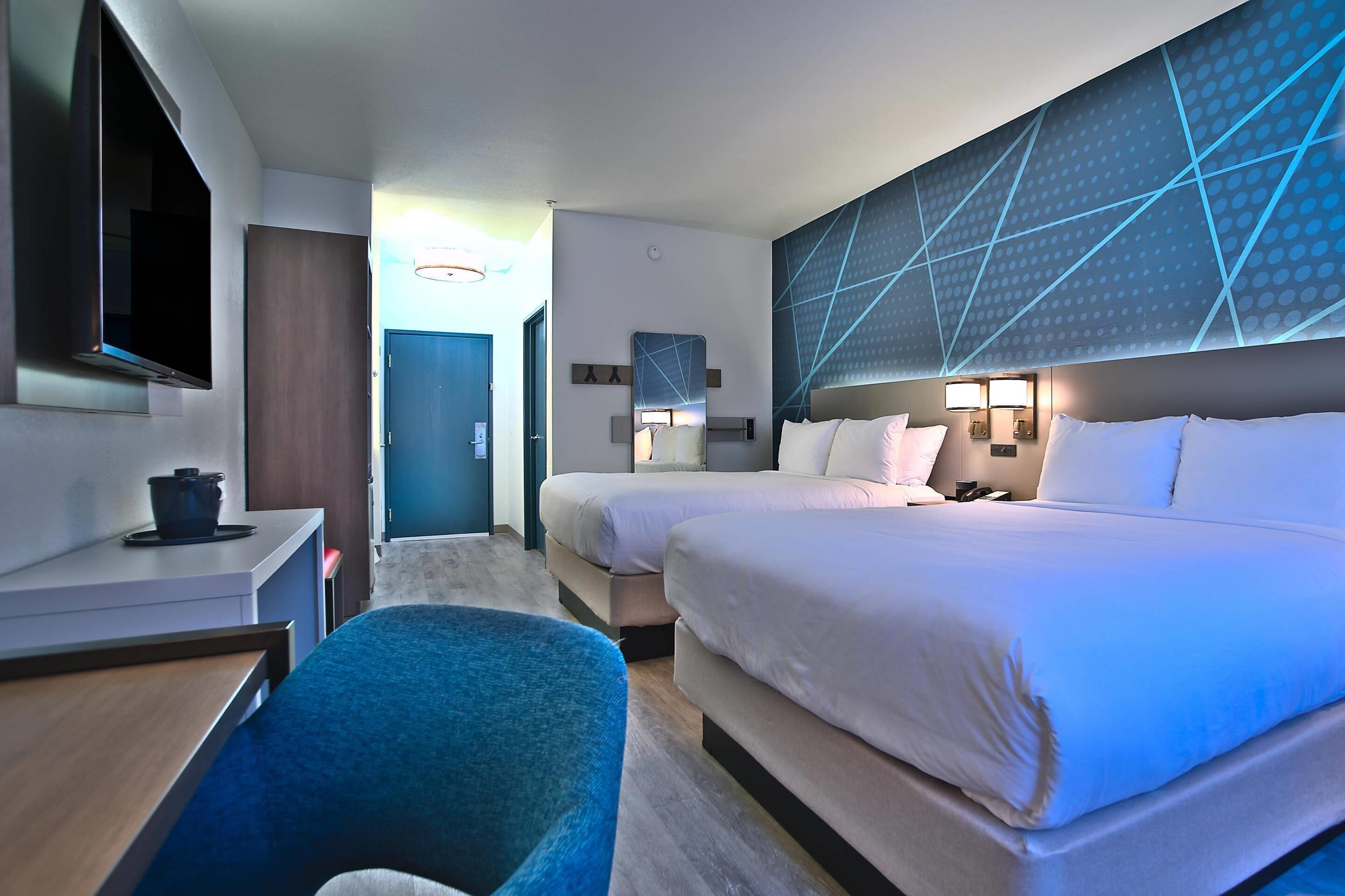 Habitación de hotel con cama, escritorio, silla, televisor y pared con diseños geométricos.