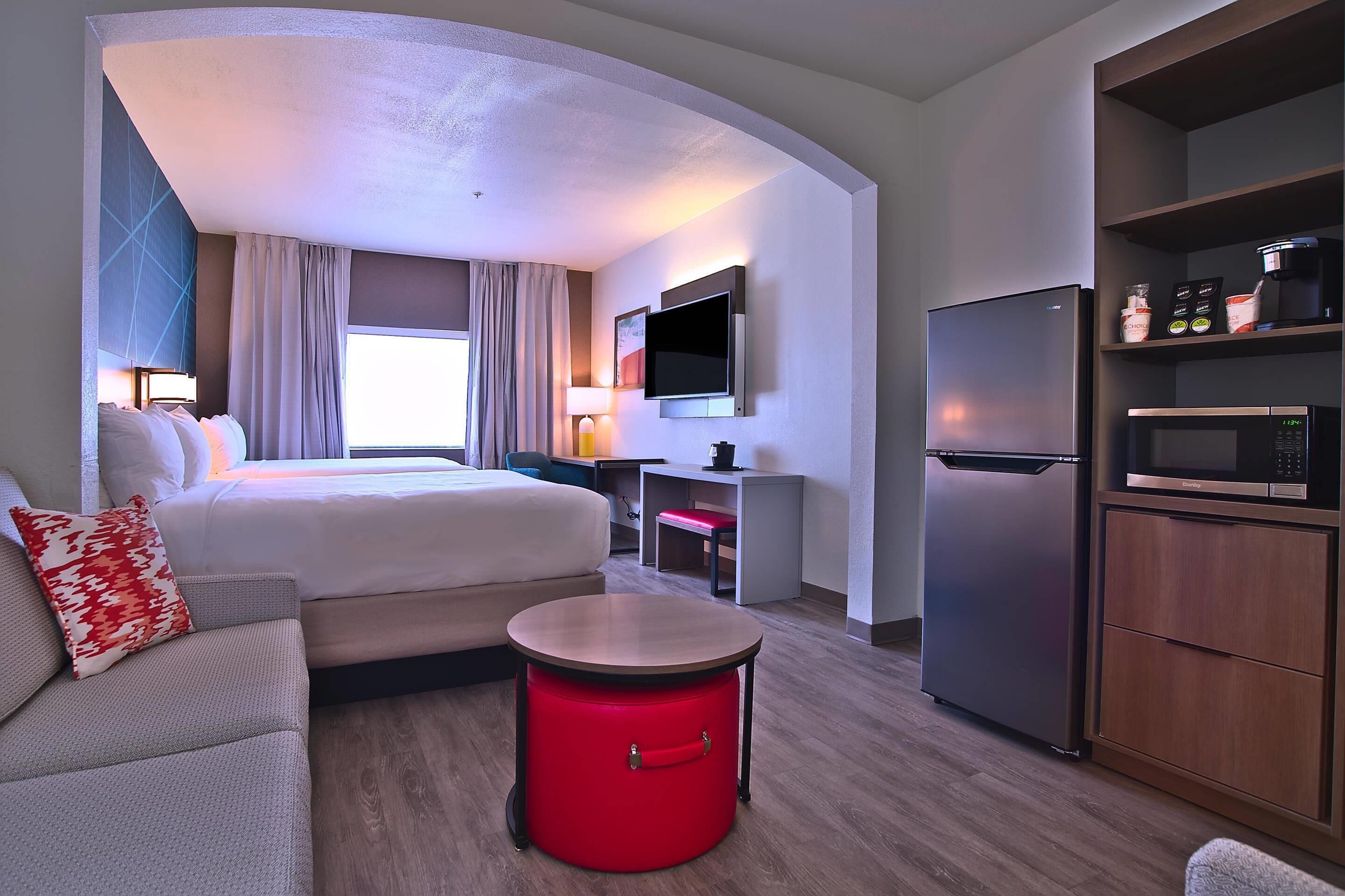 A hotel room with a bed, a red trash bin, a microwave, a refrigerator, and a TV on the wall.