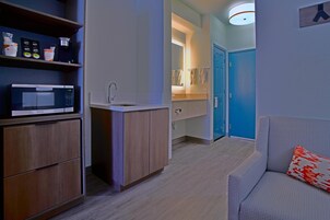 Una kitchenette funcional con microondas, lavamanos y armarios de almacenamiento.