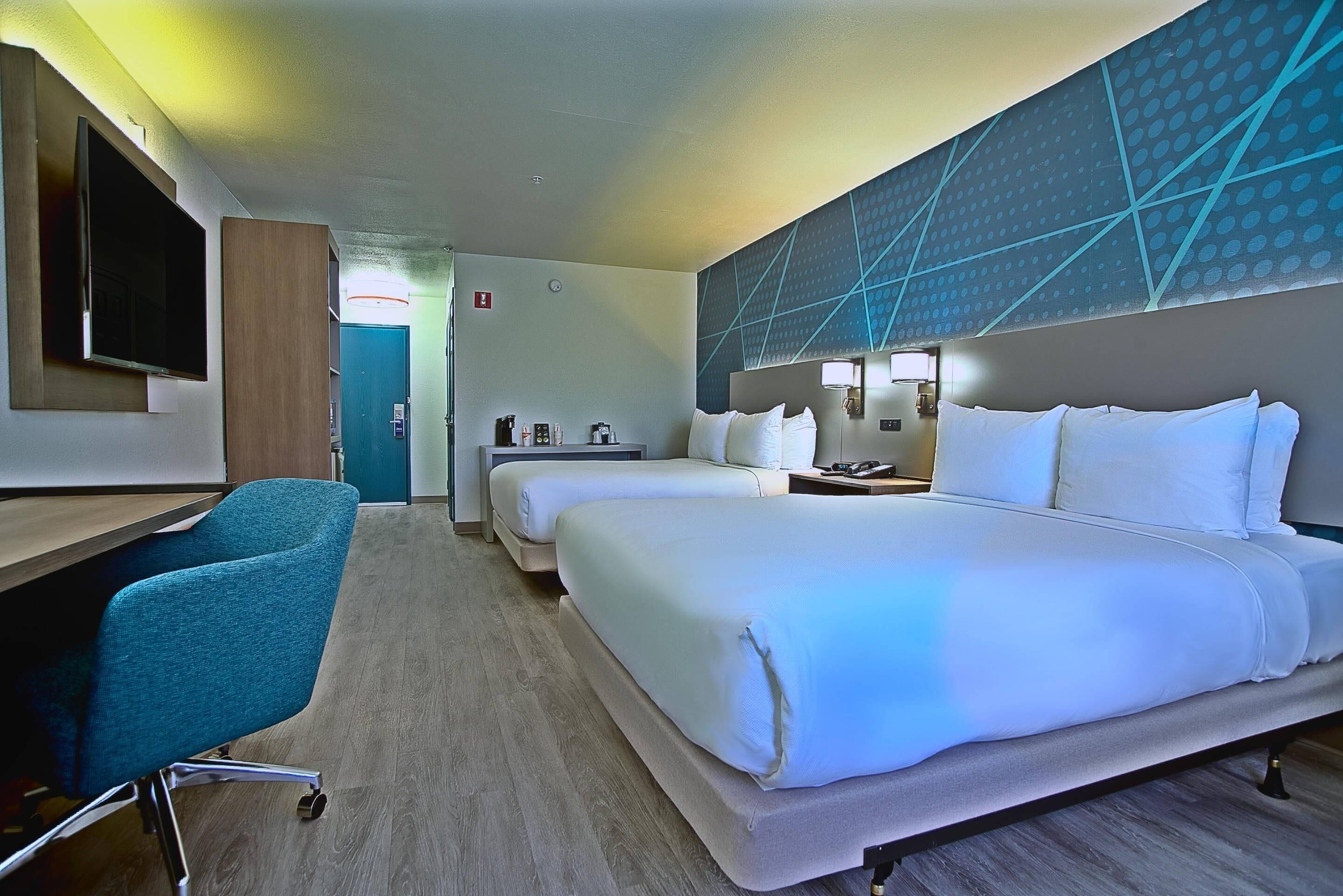 A hotel room with a desk, two beds, a TV, and a wall with a geometric pattern.