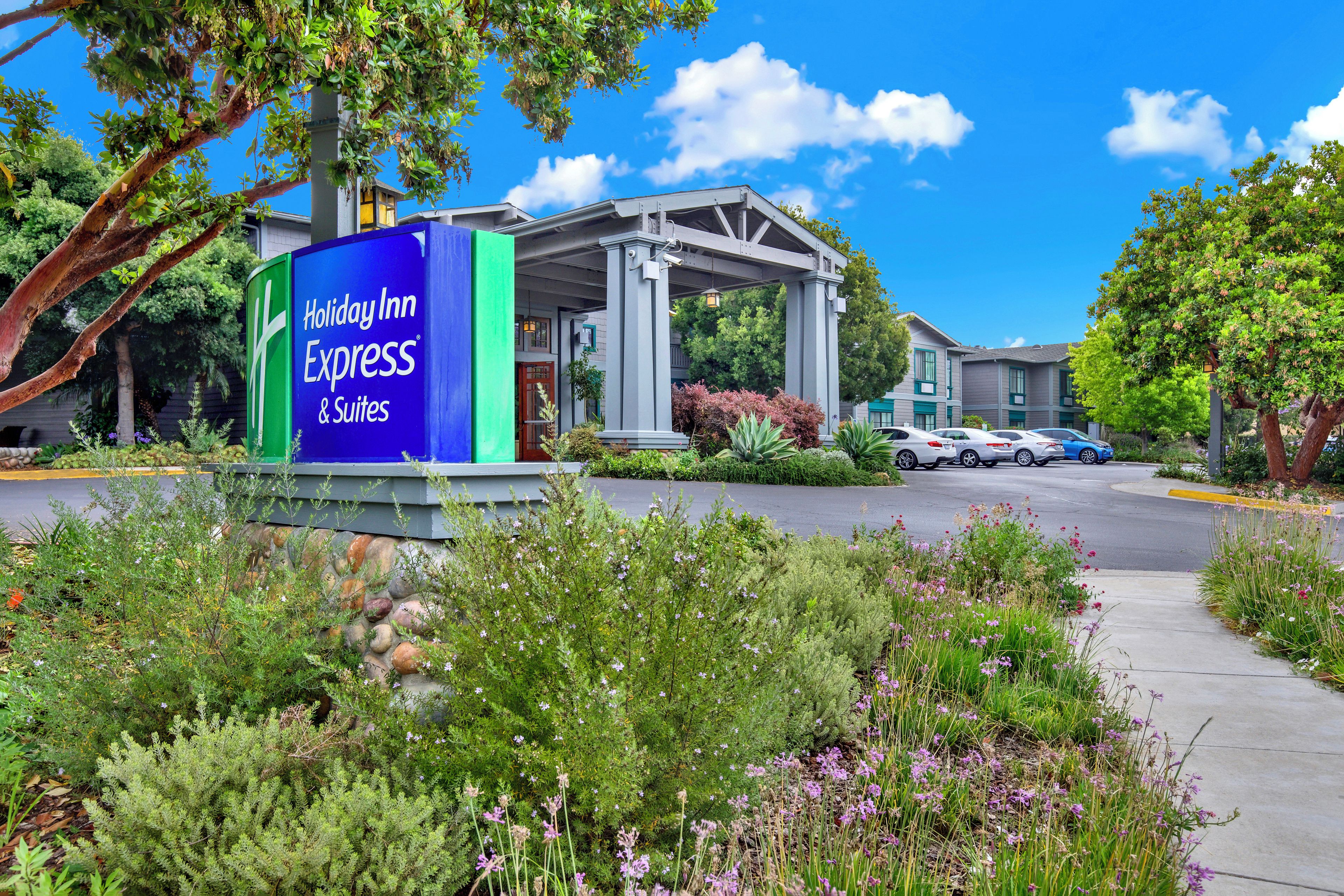 A Holiday Inn Express & Suites with a covered outdoor area, a parking lot, and a garden with various plants.