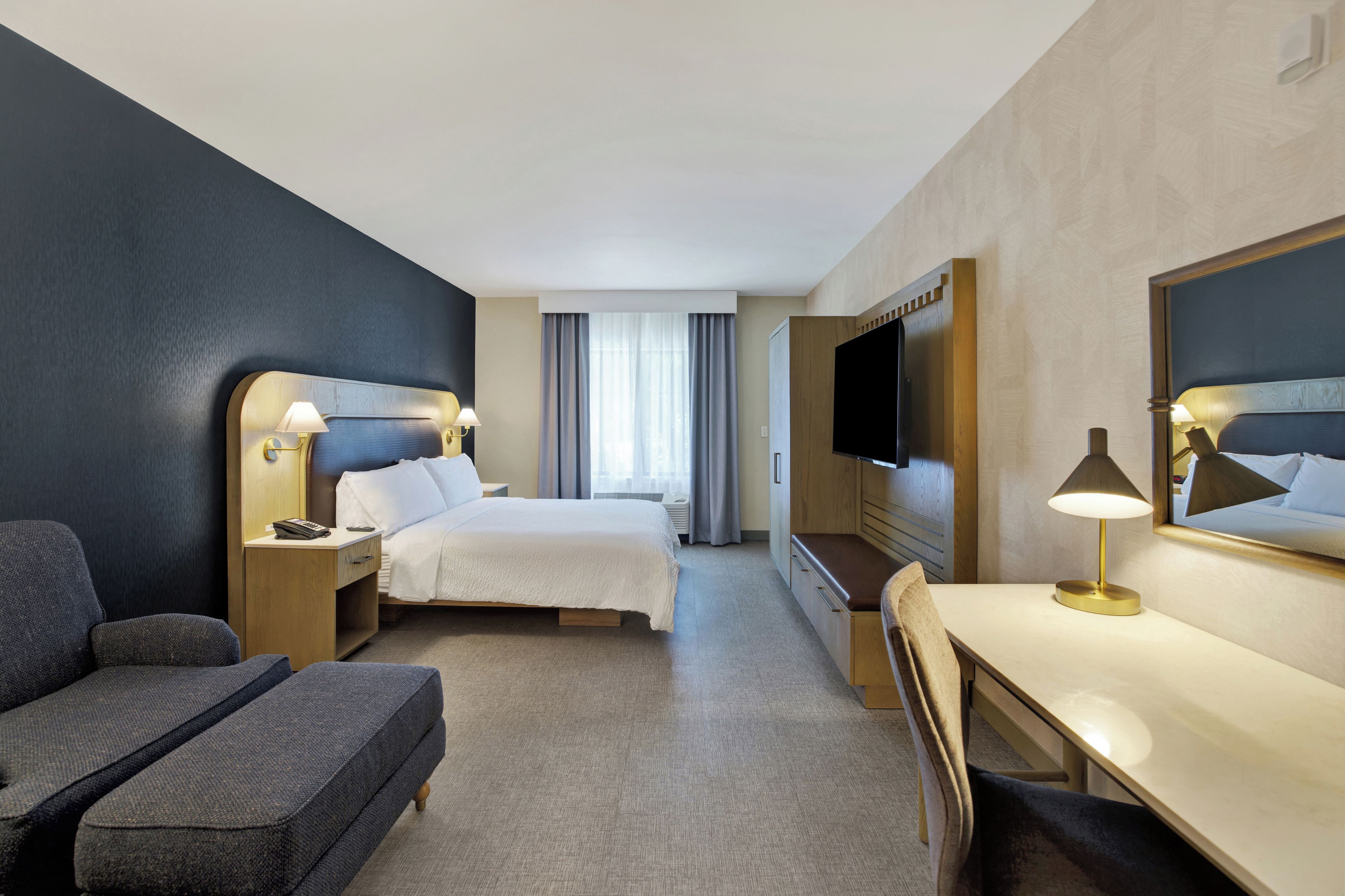Une chambre d’hôtel avec un lit, un bureau, une chaise, une télévision et une fenêtre avec des rideaux.