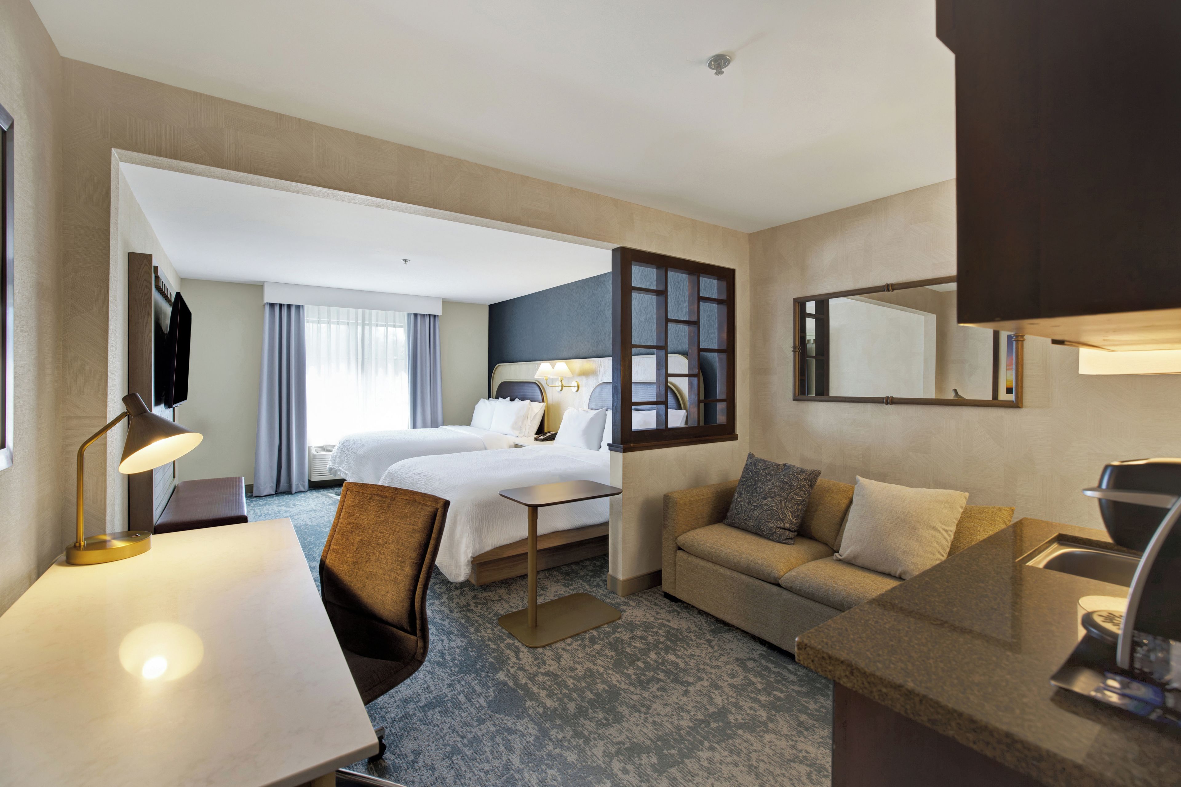 A hotel room with a bed, a sofa, a desk, and a mirror.