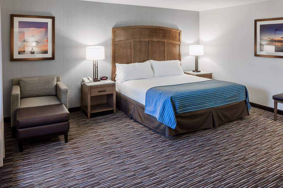 A hotel room with a bed, two bedside tables, a chair, and a carpeted floor.