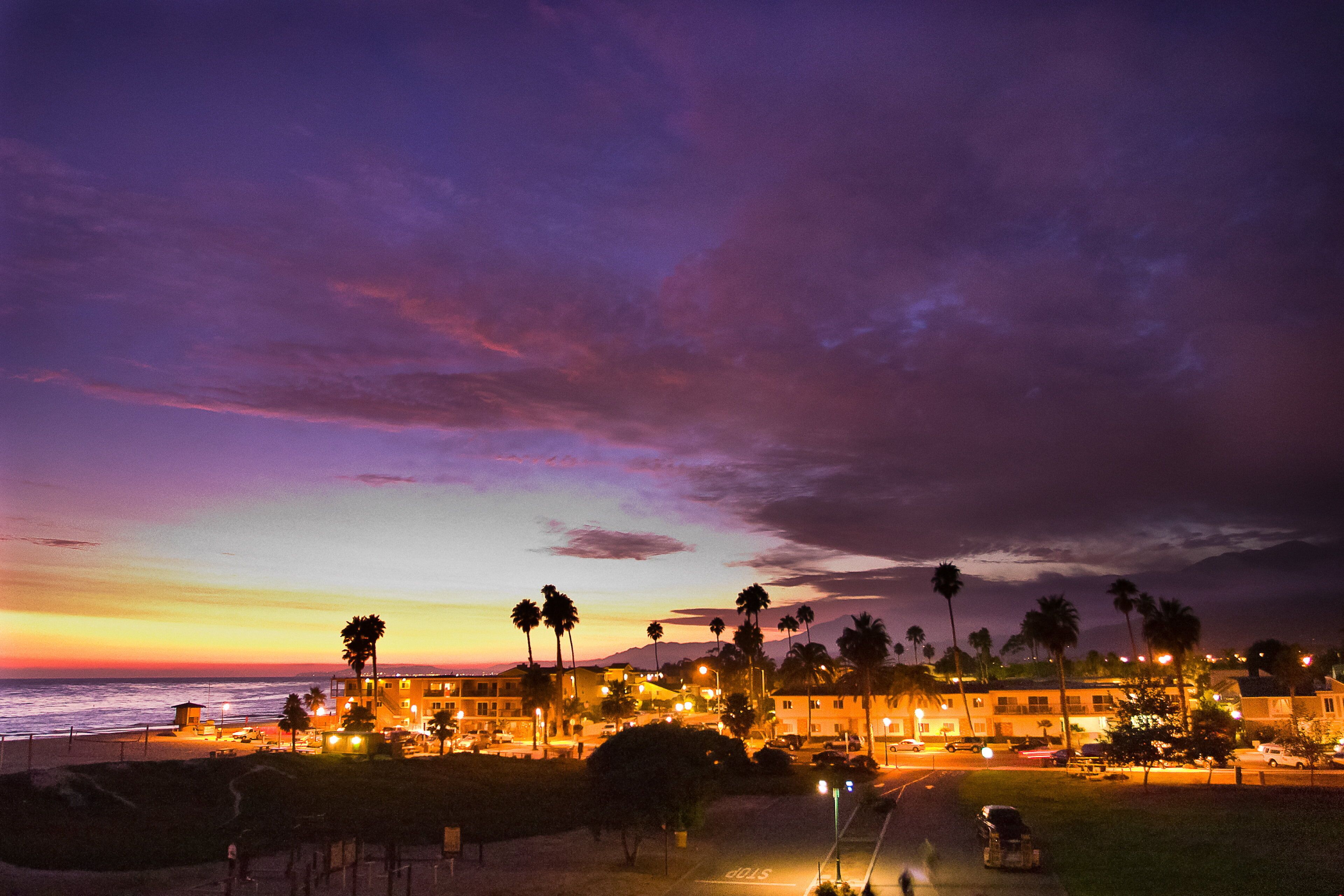 A beachfront hotel with multiple-story buildings, palm trees, and a view of the ocean.