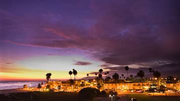 A beachfront hotel with multiple-story buildings, palm trees, and a view of the ocean.