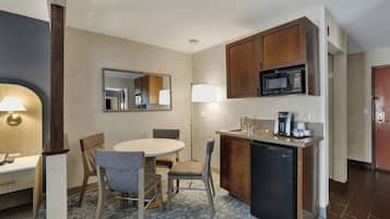A hotel room with a dining table, chairs, a microwave, a coffee maker, and a small refrigerator.