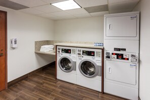 A laundry room with two front-loading washing machines, a dryer, and a towel dispenser. - Holiday Inn Express & Suites Carpinteria by IHG (Carpinteria)