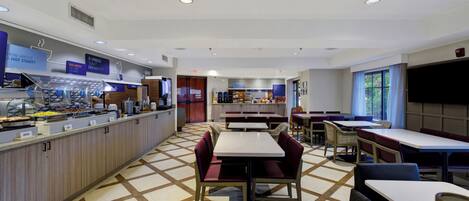 A breakfast area with a buffet, seating, and a view of the outdoors.