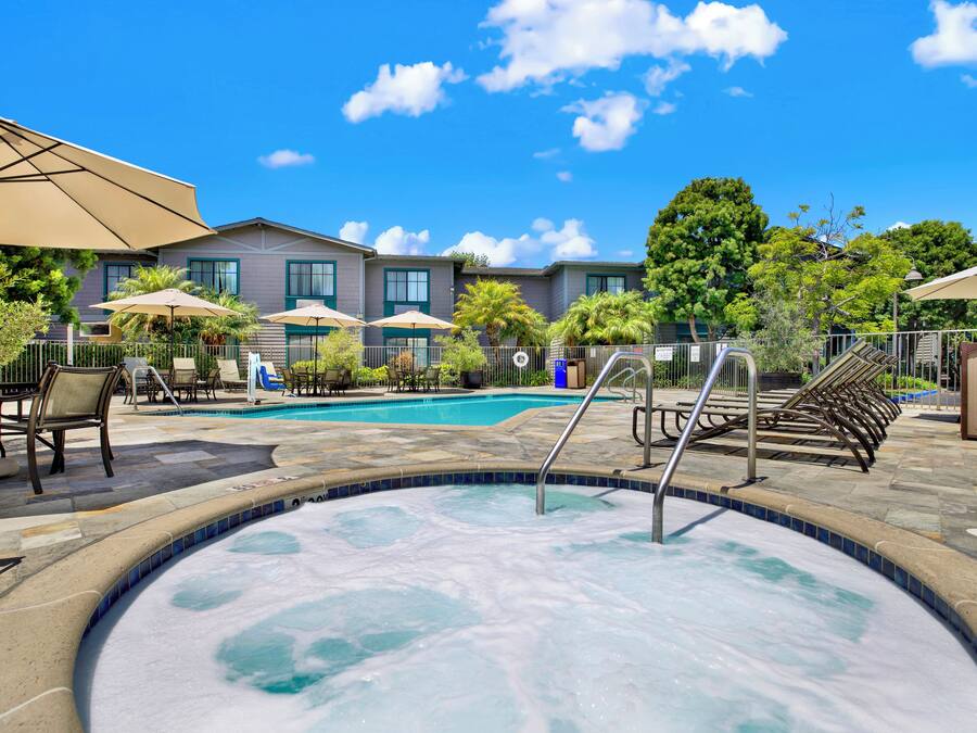 A hotel pool area with lounge chairs and umbrellas, surrounded by buildings and trees.