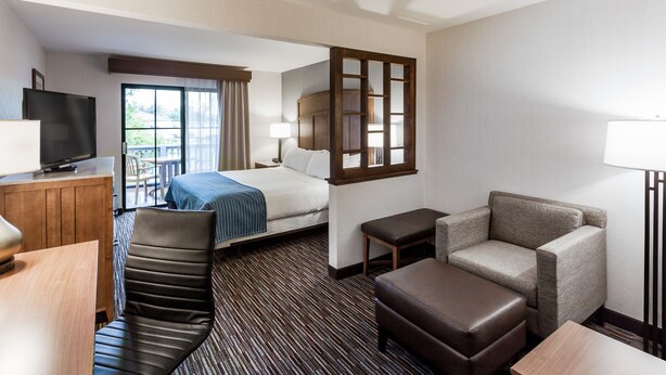 A hotel room with a bed, a desk, a chair, a sofa, a TV, and a window with curtains.