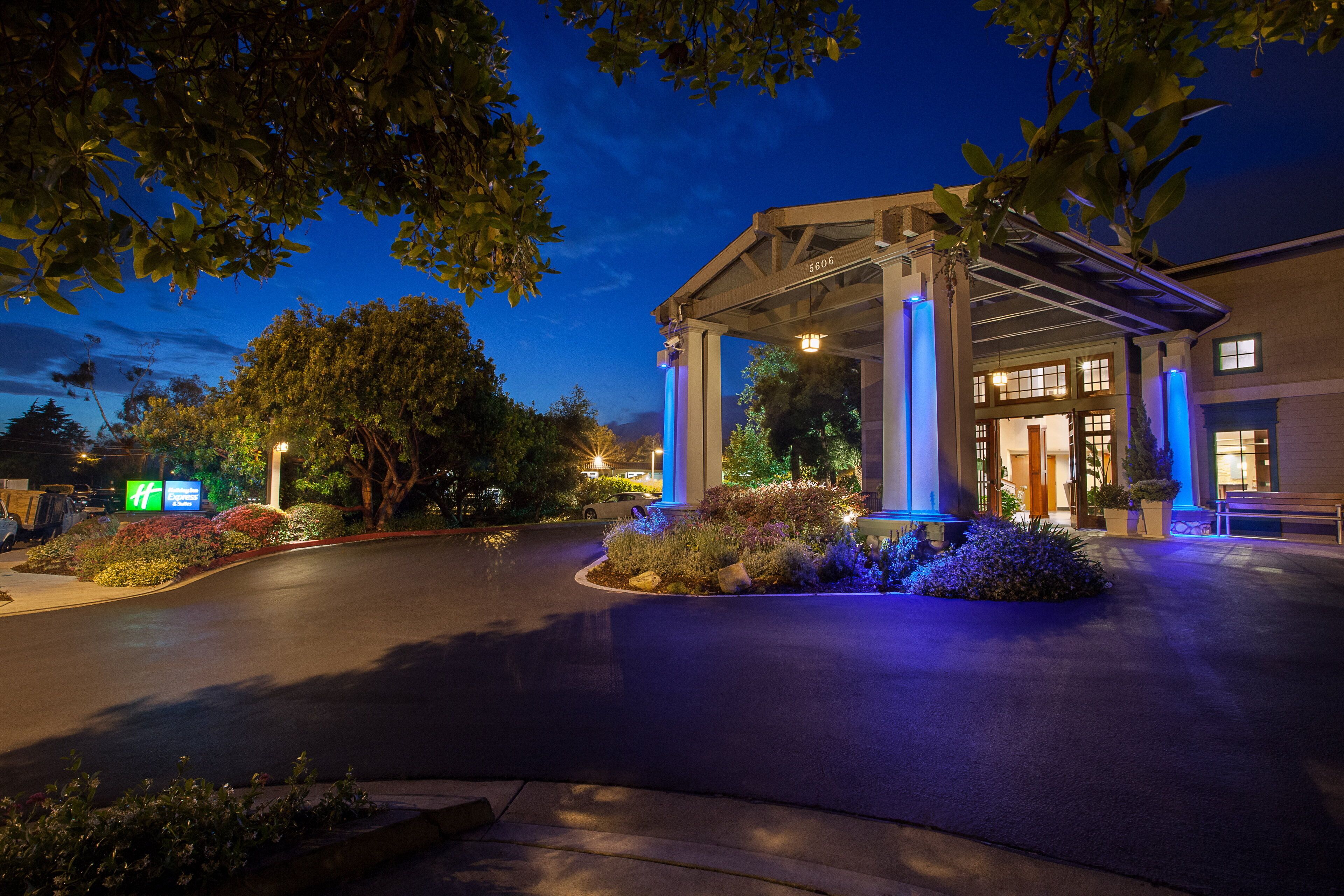 A hotel entrance with a covered walkway, a parking area, and a landscaped garden.