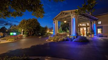 A hotel entrance with a covered walkway, a parking area, and a landscaped garden.