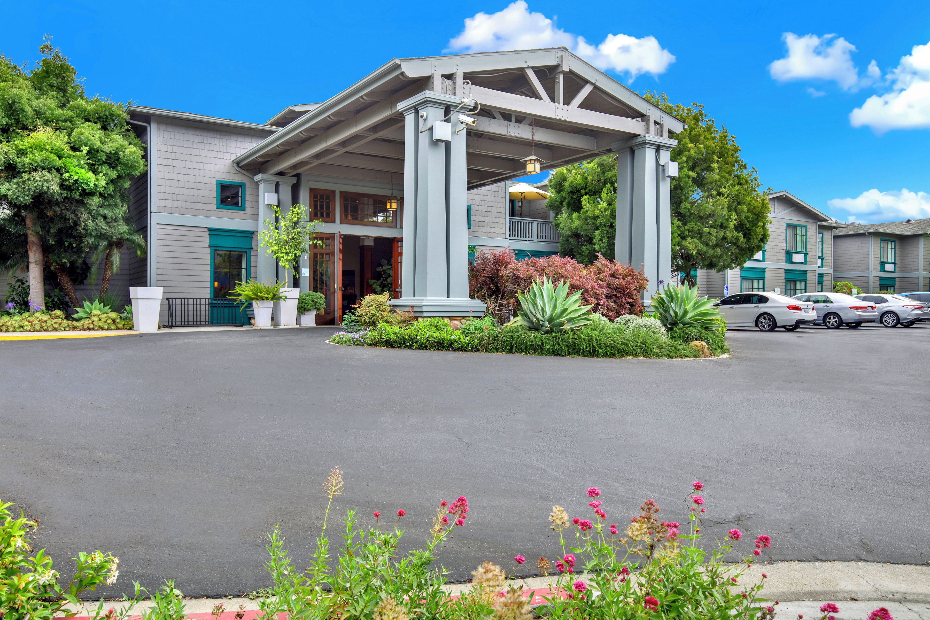 A hotel with a covered entrance, a parking lot, and a landscaped garden.