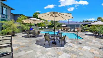 A poolside area with lounge chairs, umbrellas, and a pool.