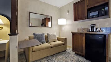 Ein gemütliches Hotelzimmer mit Küchenzeile, einer Couch mit Kissen, einem kleinen Tisch, einer Lampe und einer Mikrowelle.
