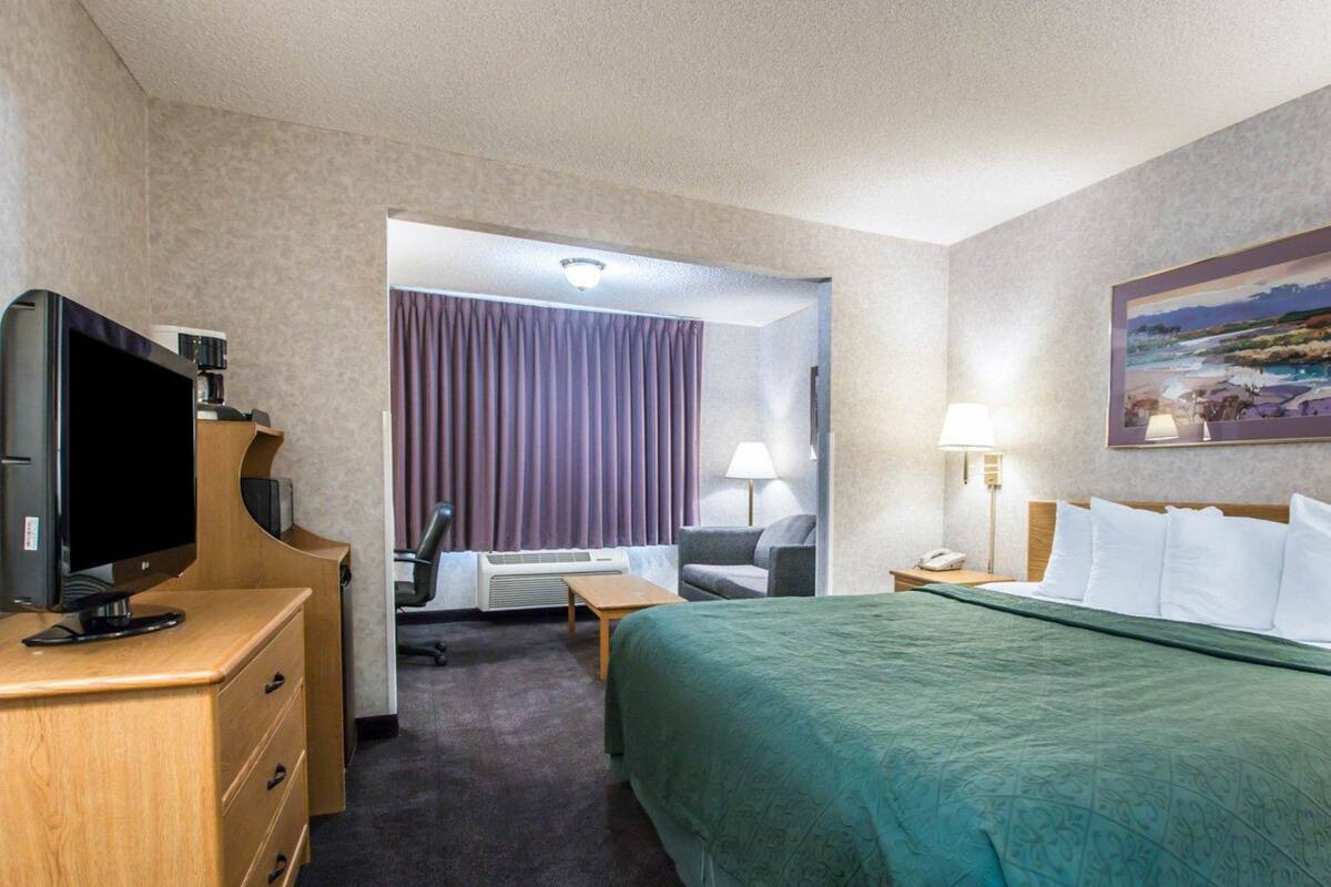Une chambre d’hôtel avec un lit, un bureau avec un ordinateur, une télévision, une chaise, une lampe et un tableau au mur.