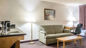 A hotel room with a kitchenette, a sofa, a coffee table, two lamps, and a painting on the wall.