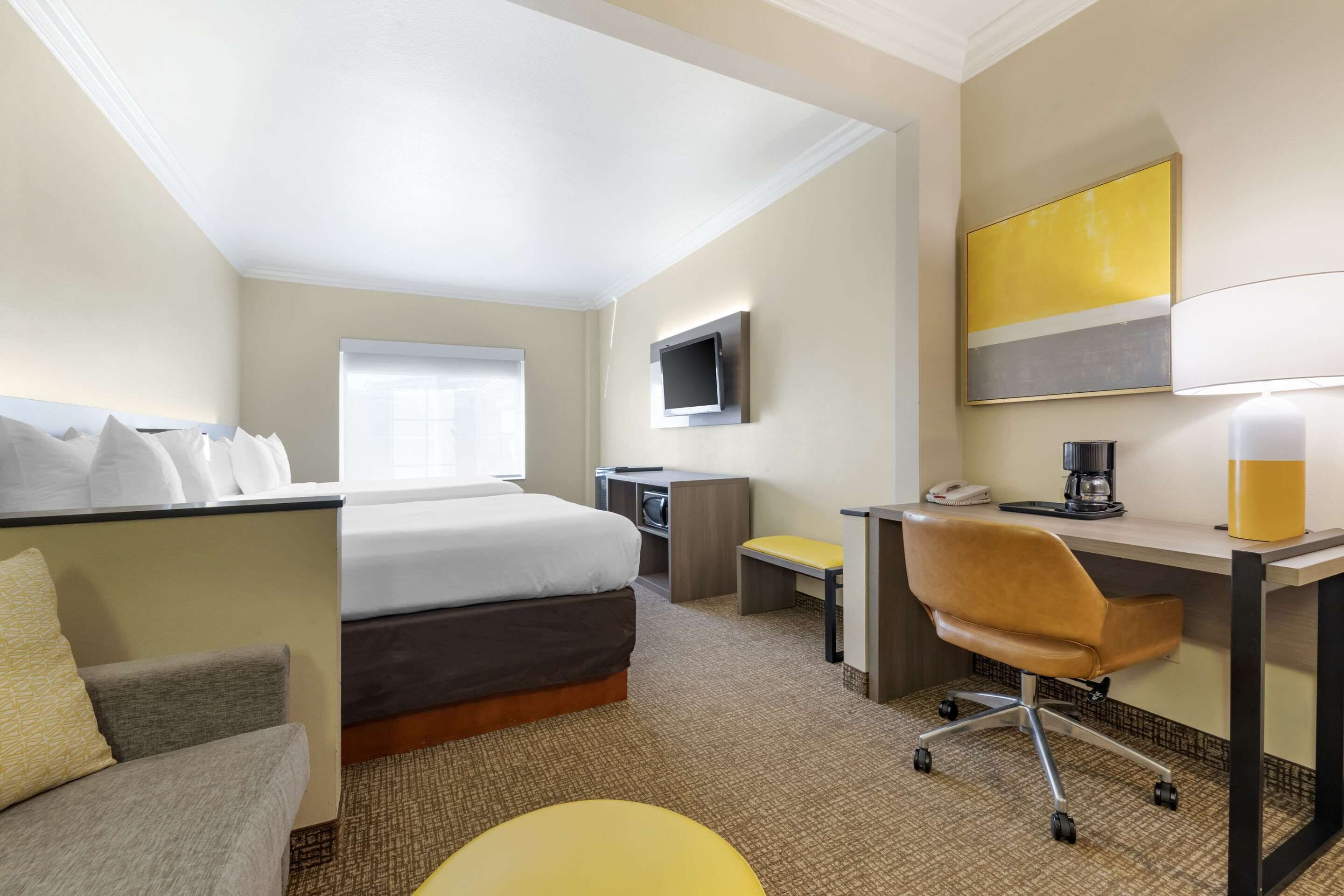 Quarto de hotel com cama, escrivaninha, cadeira, televisão e cafeteira.
