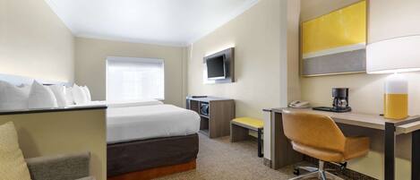 Quarto de hotel com cama, escrivaninha, cadeira, televisão e cafeteira.