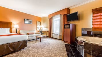 A hotel room with a bed, a sofa, a desk with a lamp, a television, a microwave, and a bathroom with a bathtub.