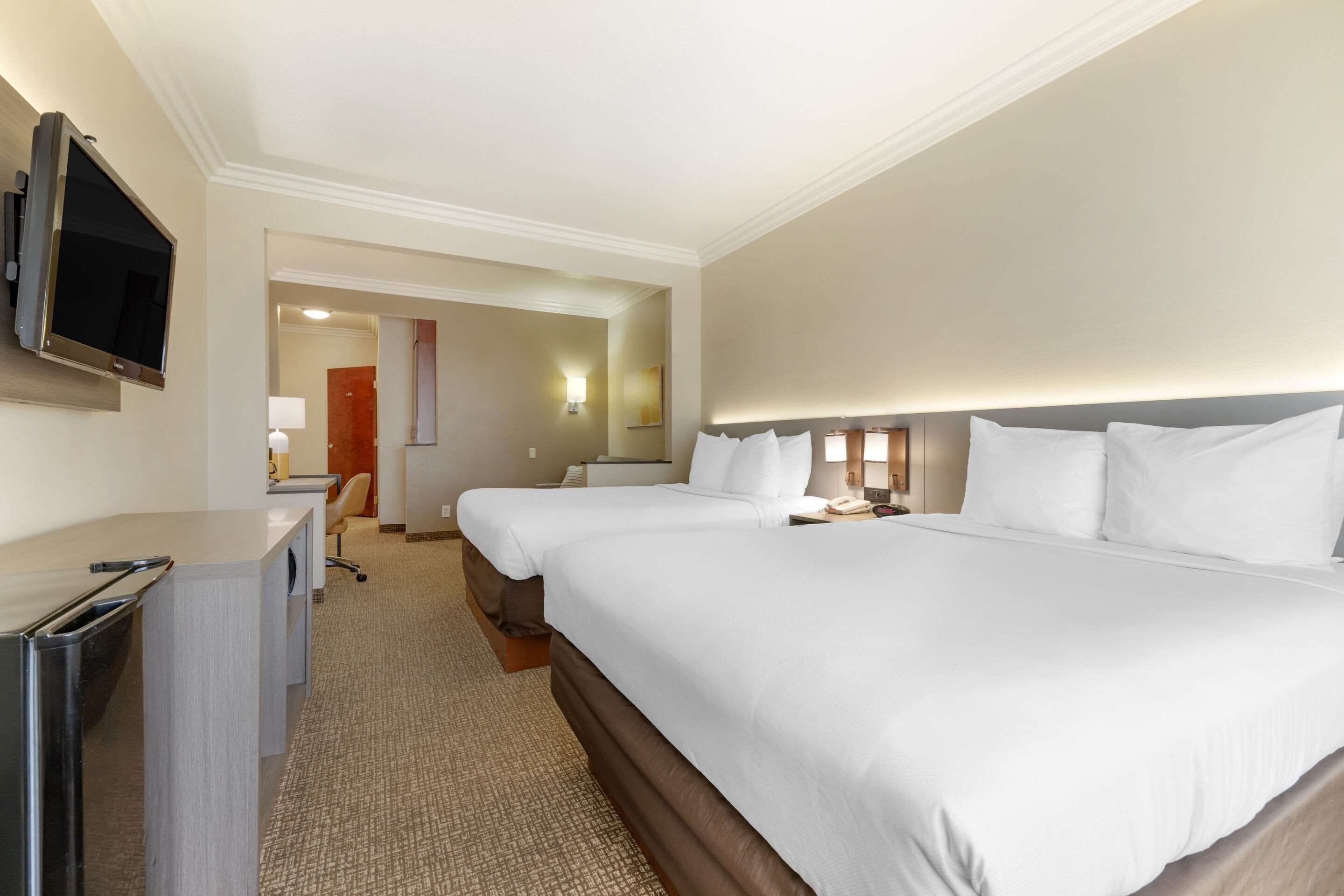 A hotel room with two beds, a desk, a television, and a bathroom visible through an open door.