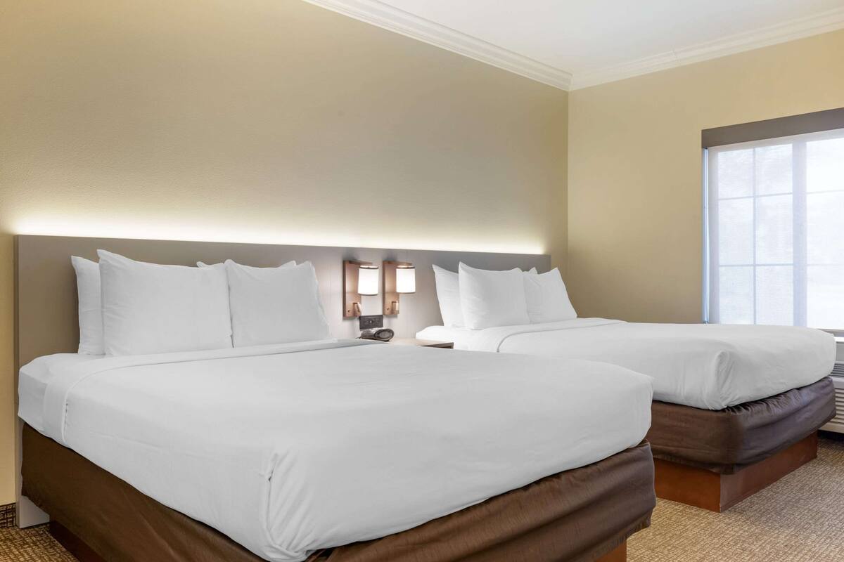 A hotel room with two beds, a large window, and a wall-mounted light fixture.