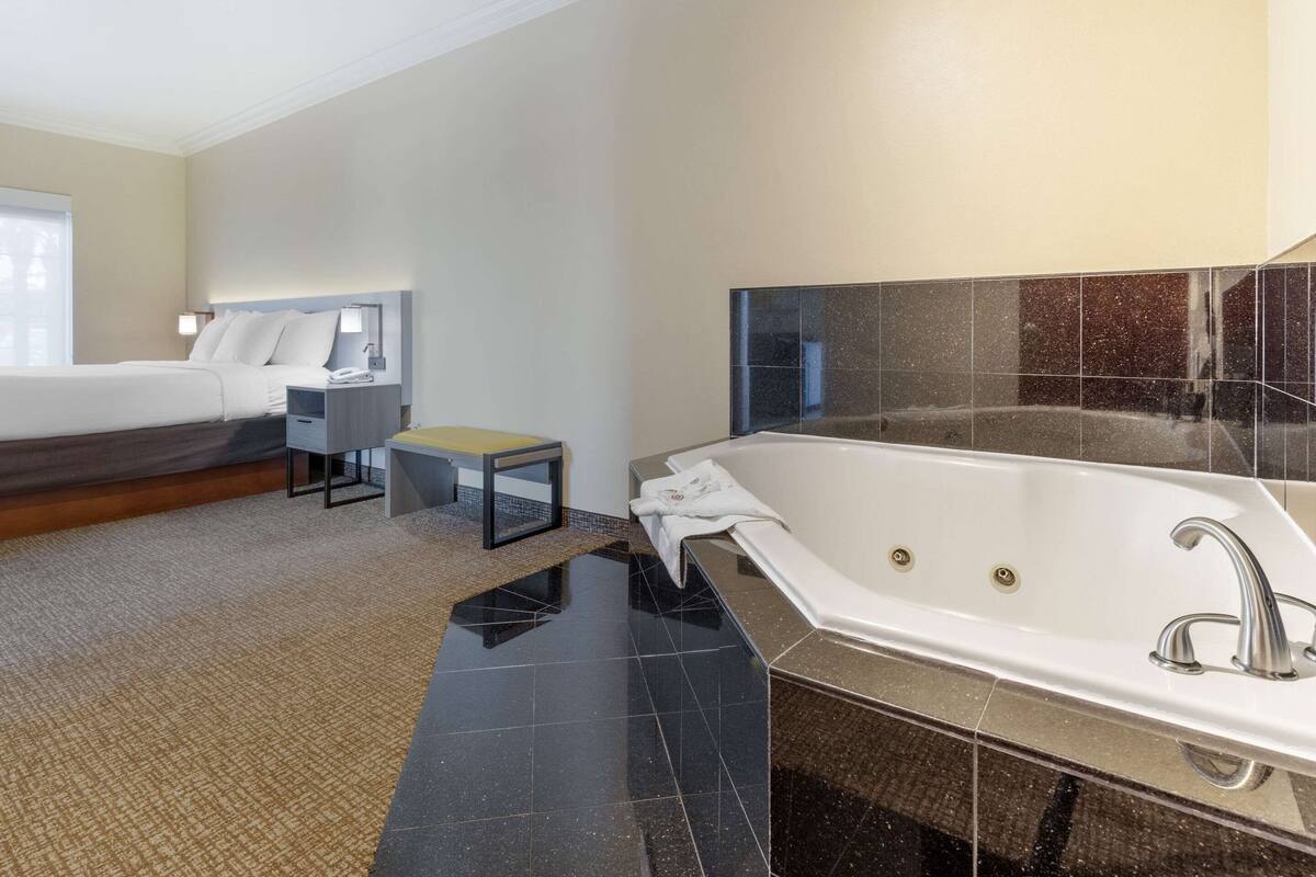 A modern hotel room with a large bed, a separate sitting area, a bathtub, and a small table.