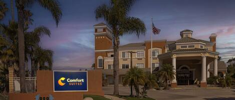 Un hôtel avec une grande enseigne indiquant « Comfort Suites » et une entrée bien visible, dotée d’un espace abrité.