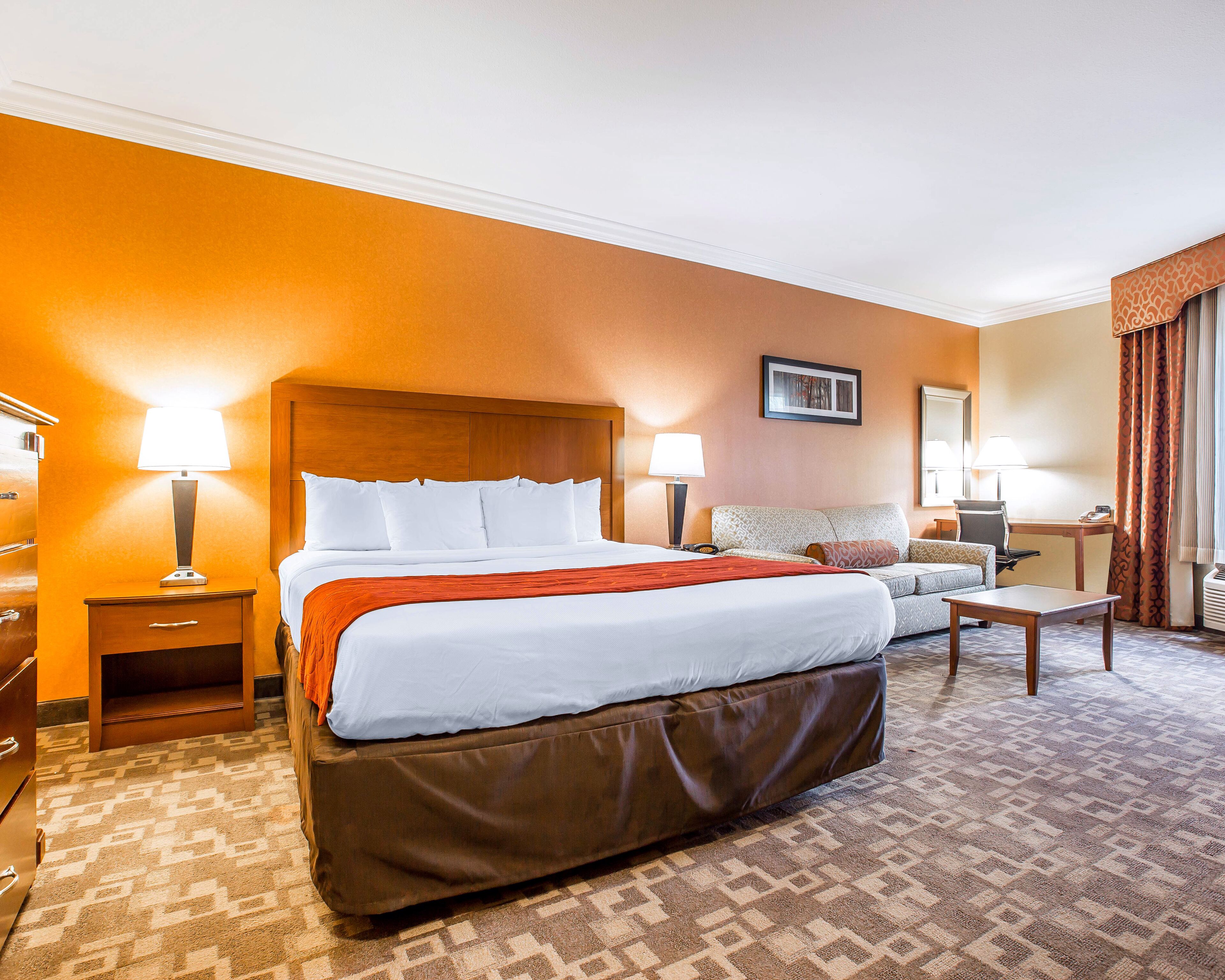 A hotel room with a large bed, a sofa, a desk, and a chair.
