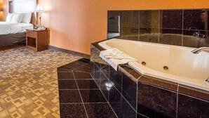 A hotel room with a large bathtub, a bed, a nightstand, and a patterned carpet. - Comfort Suites Oceanside Camp Pendleton Area (Oceanside)