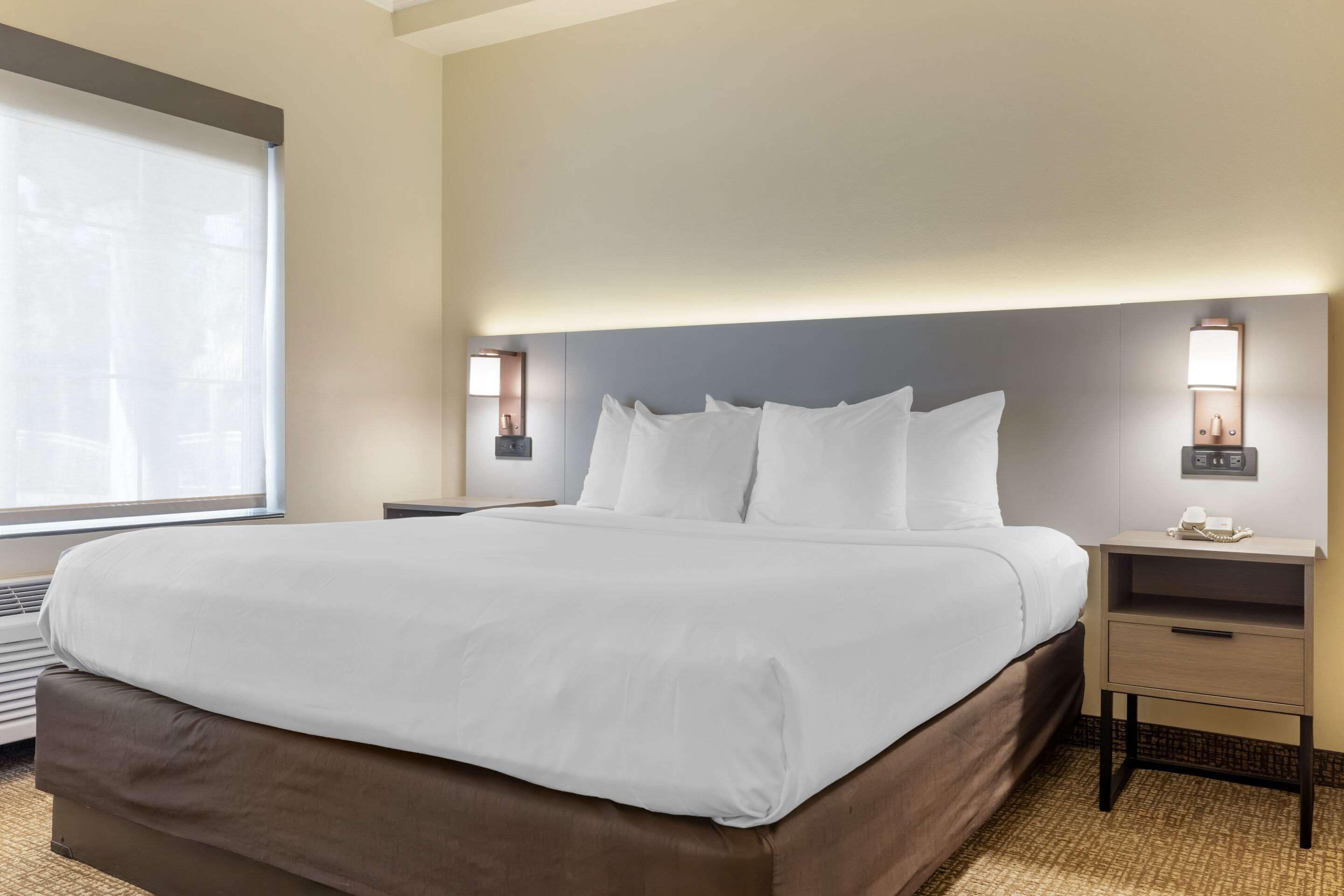 A hotel room with a large bed, bedside tables, and wall-mounted lamps.