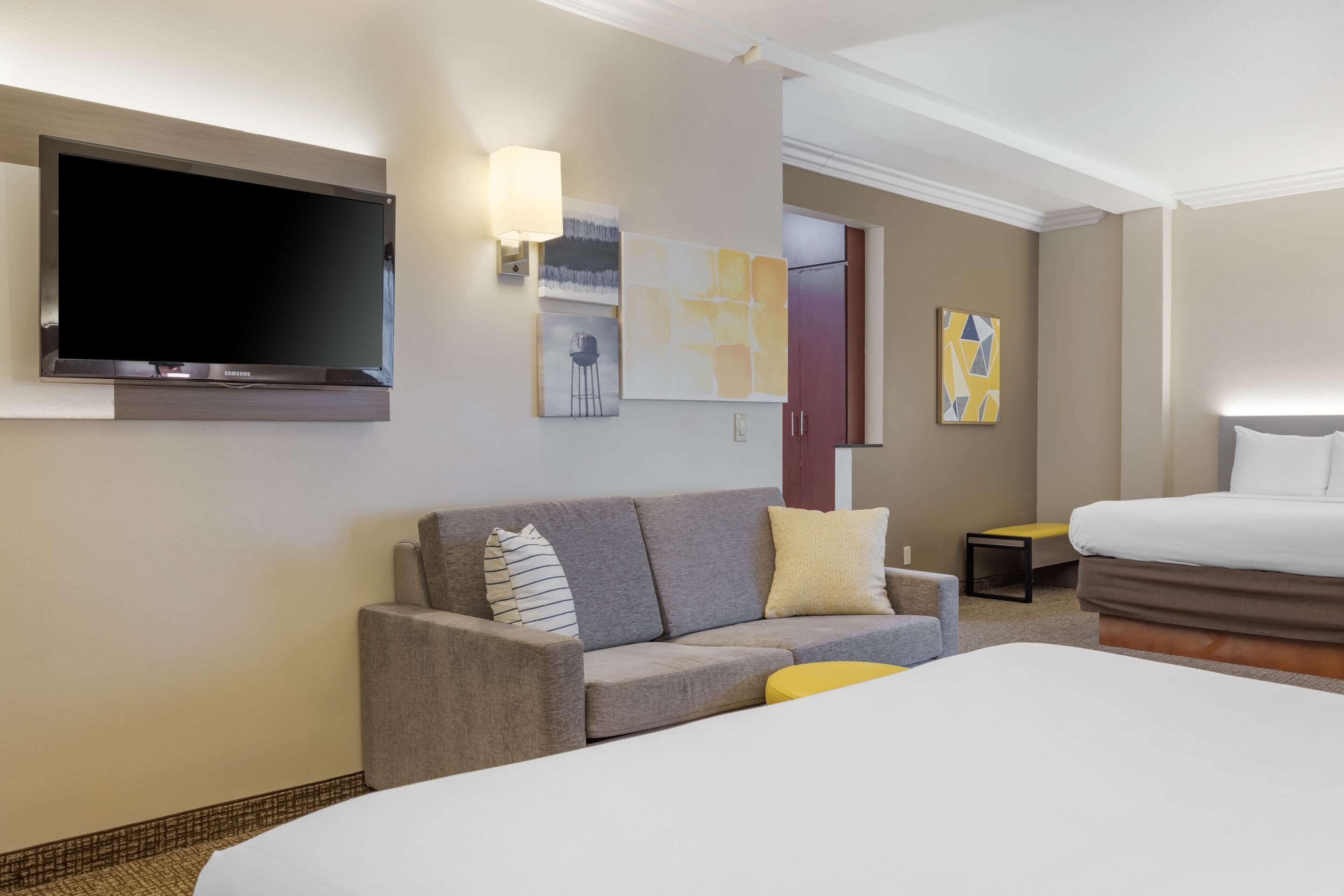 A hotel room with a bed, a sofa, a TV mounted on the wall, and artwork on the walls.