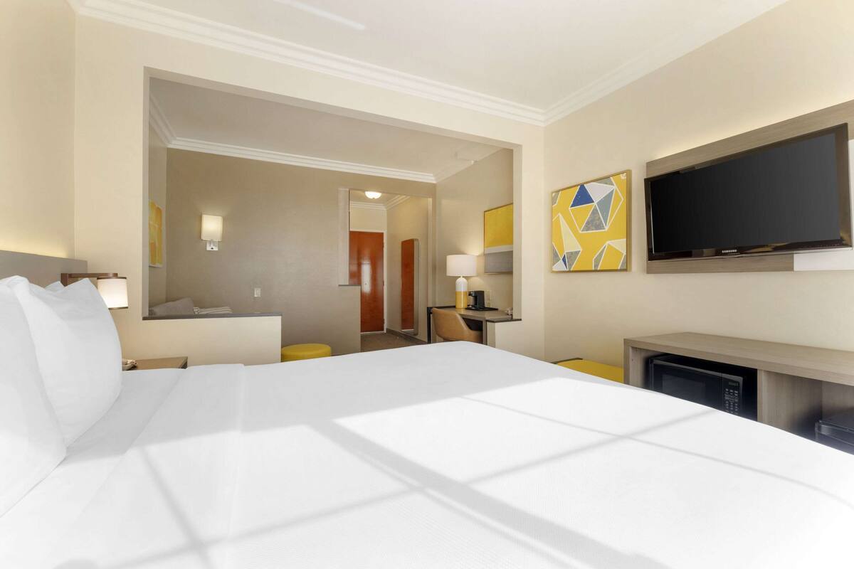 A hotel room with a large bed, a flat-screen TV mounted on the wall, a desk with a lamp, and a microwave.