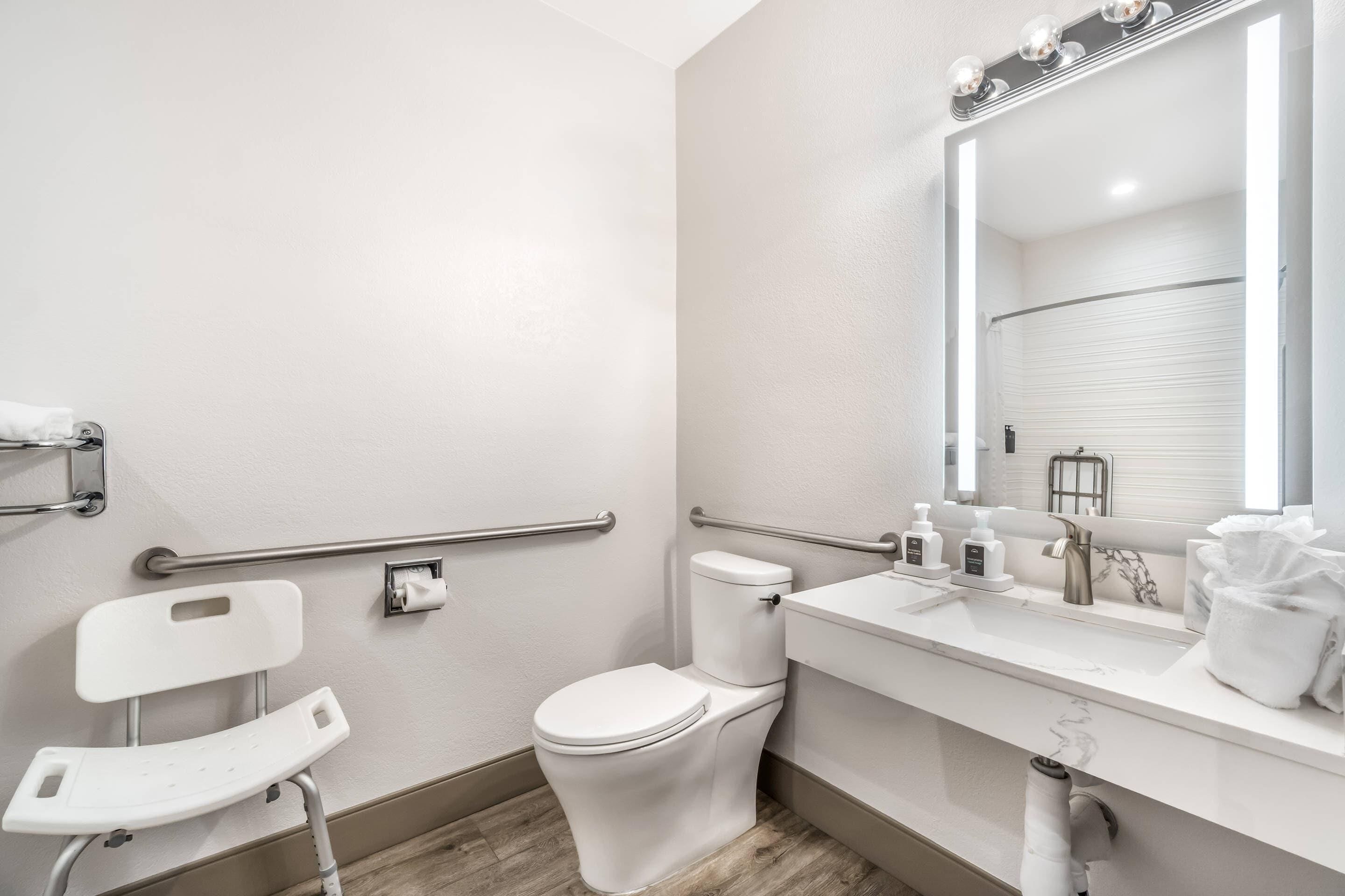 A modern bathroom with a white toilet, a vanity with a mirror, and a grab bar.