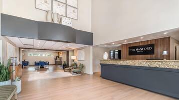 Un espace d’accueil d’hôtel au design moderne, comprenant un comptoir d’accueil, un coin salon et une vue sur la salle à manger.