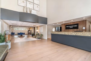 Uma área de recepção de hotel com design moderno, incluindo balcão de atendimento, espaço de estar e vista para o salão de refeições.