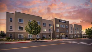 A modern hotel building with multiple floors, a prominent entrance, and a clear sky with clouds. - The Hanford Hotel, an Ascend Collection Hotel (Hanford)
